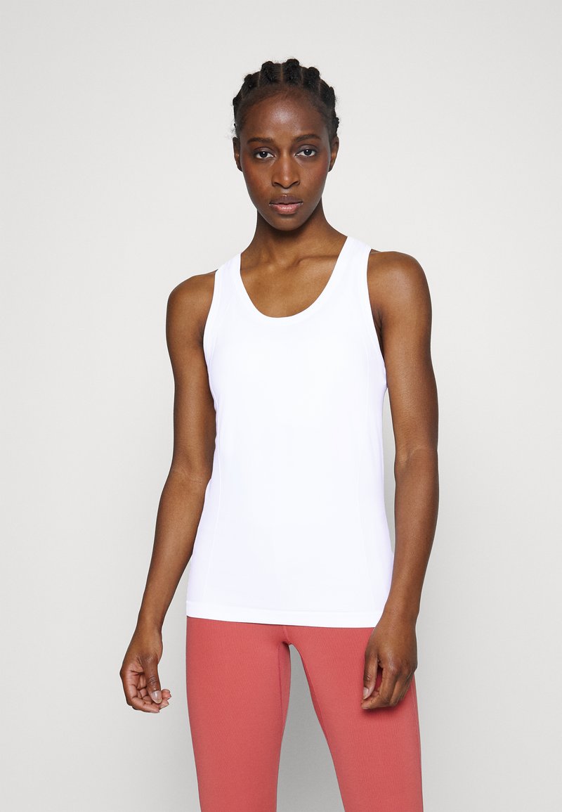 Balta bezpiedurkņu tēja, kas izgatavota no gludas, elastīgas vielas, ar apaļu kakla izgriezumu un plašām siksnām, kombinēta ar gaiši rozā ribotām legingām.