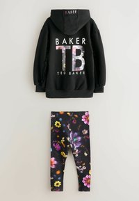 Čierna mikina s kapucňou s kvetinovým potlačou a logom "BAKER" na chrbte, v kombinácii s čiernymi legínami zdobenými farebným kvetinovým vzorom.