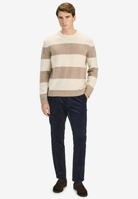 Gestreepte gebreide trui in crème en beige, met een ronde hals. Gecombineerd met donkerblauwe corduroy broek en bruine loafers.