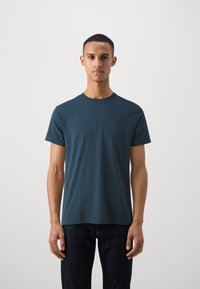Dark teal short-sleeve t-shirt with a round neckline, made of soft fabric. The fit is relaxed, paired with dark denim jeans.