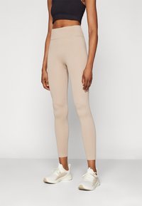 Leggings beige con canalé y cintura alta, de textura suave y diseño ajustado, combinados con zapatillas blancas con acentos claros.