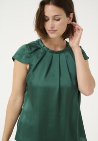 Green silk top with short cap sleeves, featuring pleats along the neckline and a smooth texture. Tailored fit with minimal detailing.