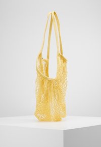 Gele nettas met twee schouderbanden, gemaakt van flexibel materiaal, met een ruim ontwerp en een open textuur.