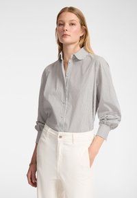 Camicia button-up con strisce verticali bianche e nere, maniche lunghe, vestibilità rilassata e colletto classico, abbinata a pantaloni bianchi.