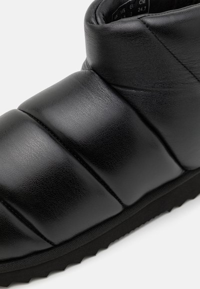 Zwarte leren enkelbottines met gevoerde secties en een gestructureerde afwerking. Voorzien van een rubberen zool met zigzagprofiel voor grip.