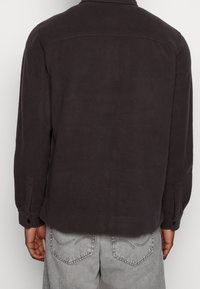Giacca camicia grigia scura a maniche lunghe, texture morbida, polsini con bottoni, dettaglio di cucitura sottile sulle spalle, vestibilità casual.