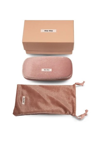 Il packaging di Miu Miu include una custodia per occhiali in velluto rosa e una sacca con coulisse coordinata, posizionate sopra una scatola di cartone beige.
