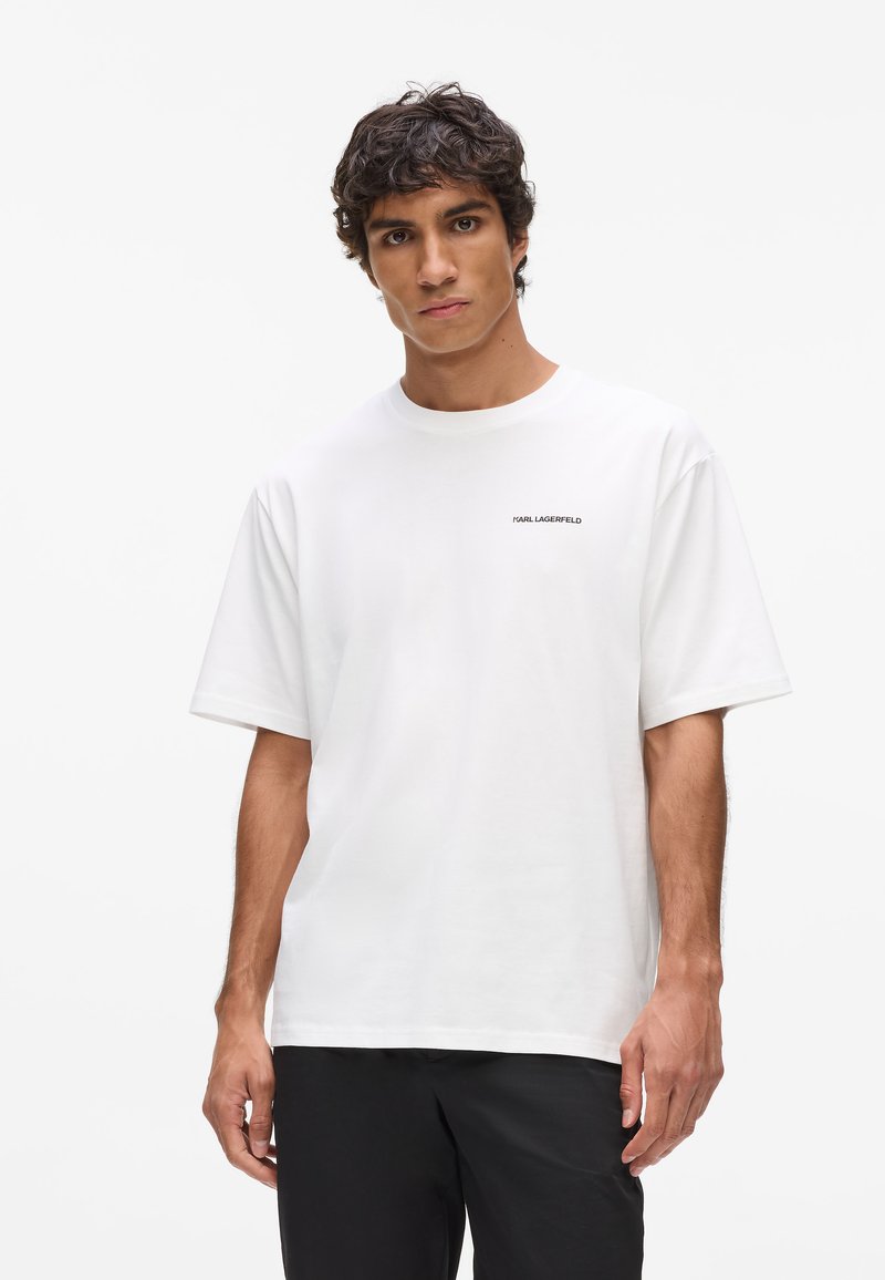 Biela krátkoprstá tričko vyrobené z bavlny. Má okrúhly výstrih a malé čierne logo na ľavej hrudi. Hladká textura, uvoľnený strih.