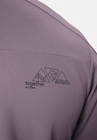 Tissu violet respirant avec un motif imprimé de trois contours de montagne et le texte "ensemble là-bas" au dos d'un vêtement.