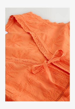 Orange bomuldsbeklædning med broderede bladmotiver, bølgede kanter og bindelukning foran. Blød tekstur med indviklede detaljer.