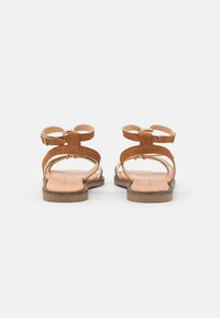 Tanschoenen van leer met een open ontwerp, voorzien van twee banden en strikken aan de achterkant. Platte zolen met minimale grip.