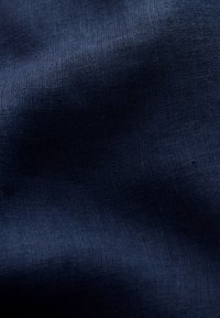 Tissu bleu foncé avec une texture de tissage fine visible et des plis doux créant des ombres subtiles et de la profondeur.