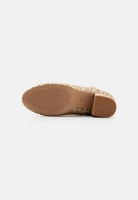 Glitrende gull slip-on sko med en teksturert overflate og en glatt, tan gummisåle. Skoen har en buet form og en lav hæl.