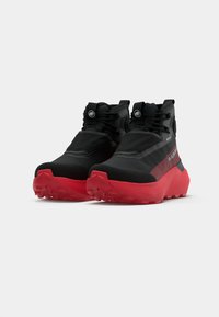 Schwarze und rote High-Top-Schuhe mit einer strukturierten Oberseite, verstärkter Zehenpartie, großen Schnürsenkeln und einer Sohle mit tiefen Profilen für den Grip.