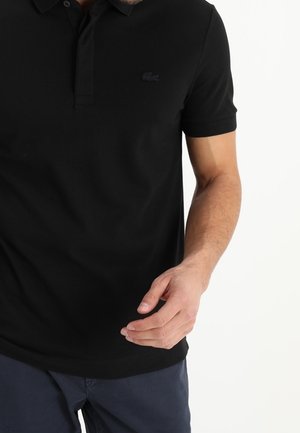 Polo noir en coton, avec un col classique, des manches courtes et un logo noir brodé discret sur la poitrine.