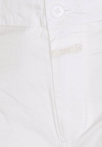 Vit tyg med en slät textur, med en knappstängning och en liten klädlapp sydd i sido sömmen.