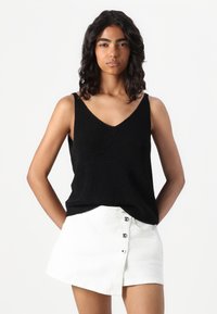 Musthave V-kaelusega must tank top, millel on sooniline tekstuur, koos valge mini seelikuga, millel on nööpdetailid ja kerge A-line lõige.