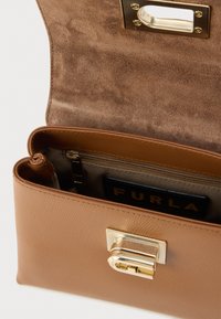 Tādas krāsas ādas soma ar gludu virsmu un zelta tonīšu aizdari. Iekšpusē ir rāvējslēdzēja kabata un zīmola kartes turētājs. Soma ir atvērta skats.