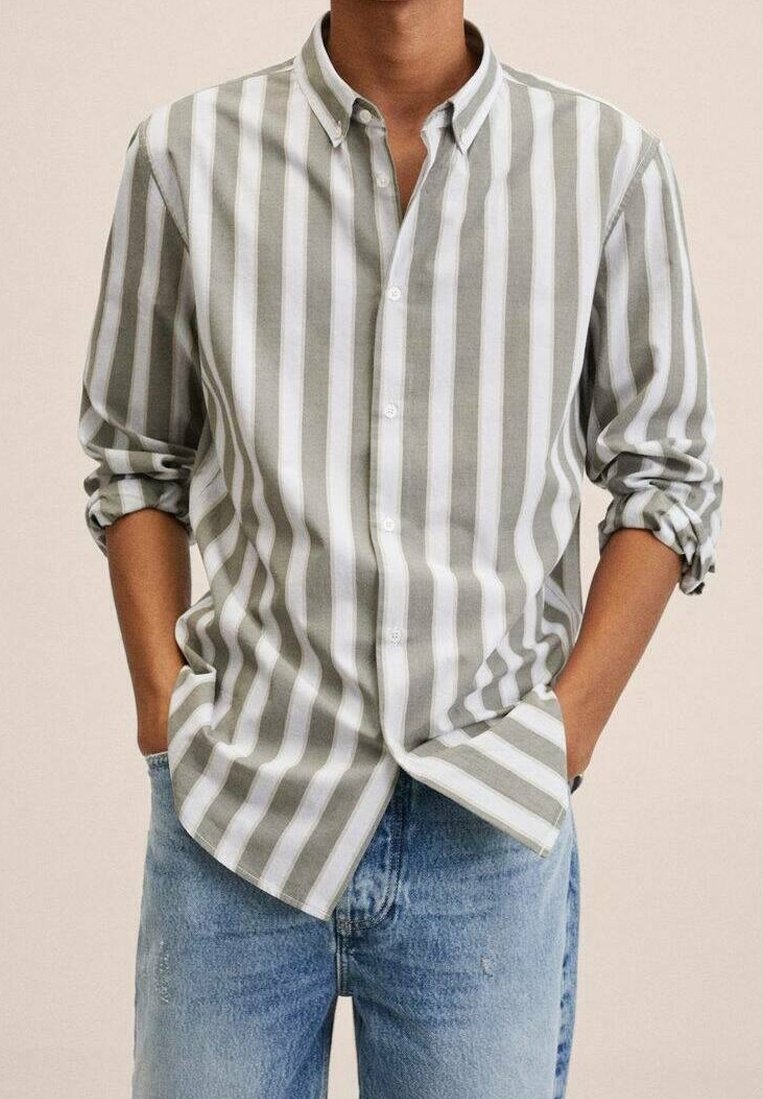 Camicia a righe grigie e bianche con colletto, maniche arrotolate e vestibilità rilassata, abbinata a jeans blu chiaro.