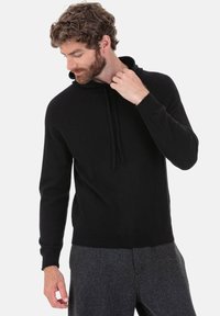 Schwarzer Kapuzenpullover aus weichem Stoff mit Kordelzug, gerippten Bündchen und Saum. Getragen zu grauen Hosen, zeigt einen lässigen Sitz.