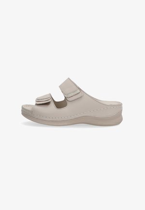 Beige leren slipper met twee verstelbare klittenbandriemen, gebogen ontwerp en een gevoerde zool met antislip oppervlak.