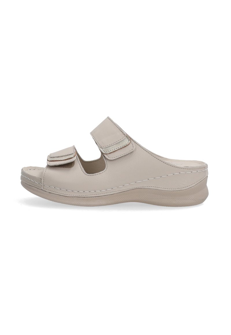 Beige leren slipper met twee verstelbare klittenbandriemen, gebogen ontwerp en een gevoerde zool met antislip oppervlak.