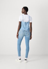 Light blue denim overalls with adjustable straps, paired with a white t-shirt and light blue skinny jeans. White sneakers with black accents.