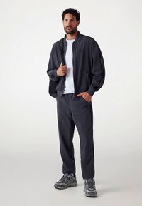 Completo sportivo da uomo composto da una giacca bomber grigio scuro e pantaloni affusolati abbinati, realizzati in materiale leggero con dettagli logo. Scarpe da ginnastica grigie completano il look.