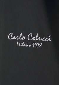 Zwarte stof met witte geborduurde tekst "Carlo Colucci Milano 1978", met een gladde textuur en een schoon, elegant ontwerp.