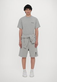 Grå kortermet T-skjorte med "NoProblemo" trykket i svart, kombinert med matchende shorts. En hettegenser er knyttet rundt livet. Hvite sneakers.