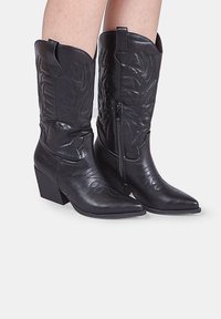 Černé kovbojské boty s špičatou špičkou a blokovým podpatkem. Obsahují embosované vzory listů a vnitřní zip pro snadné nazouvání.
