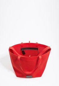 Rode mesh strandtas met dubbele stevige handvatten en een ritsvak aan de binnenkant. Heeft een gladde textuur en een ruime, open ontwerpe.