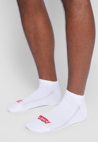 Weiße Knöchelsocken aus Baumwollmischung, mit einem roten Levi's-Logo an der Seite, gerippten Bündchen und glatter Textur.