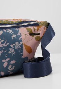Sac en tissu à motif floral avec fermeture éclair bleu marine et sangle réglable bleu marine, affichant une petite étiquette noire avec le texte "MAKE AN ENTRANCE".