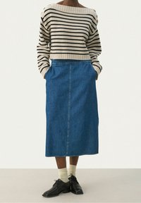 Raidallinen beige-musta neulepusero, jossa on resorireuna, yhdistetty siniseen farkkumittahameeseen, jossa on sivutaskut, sekä mustat kengät ja vaaleat sukat.