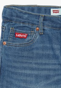 Jeans de mezclilla azul Levi's con diseño clásico de cinco bolsillos, remaches de cobre y etiqueta roja en el bolsillo frontal; textura suave.