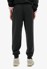 Sorte joggingbukser har en afslappet pasform med elastiske manchetter og talje. Båret med beige sneakers ser teksturen blød og afslappet ud.