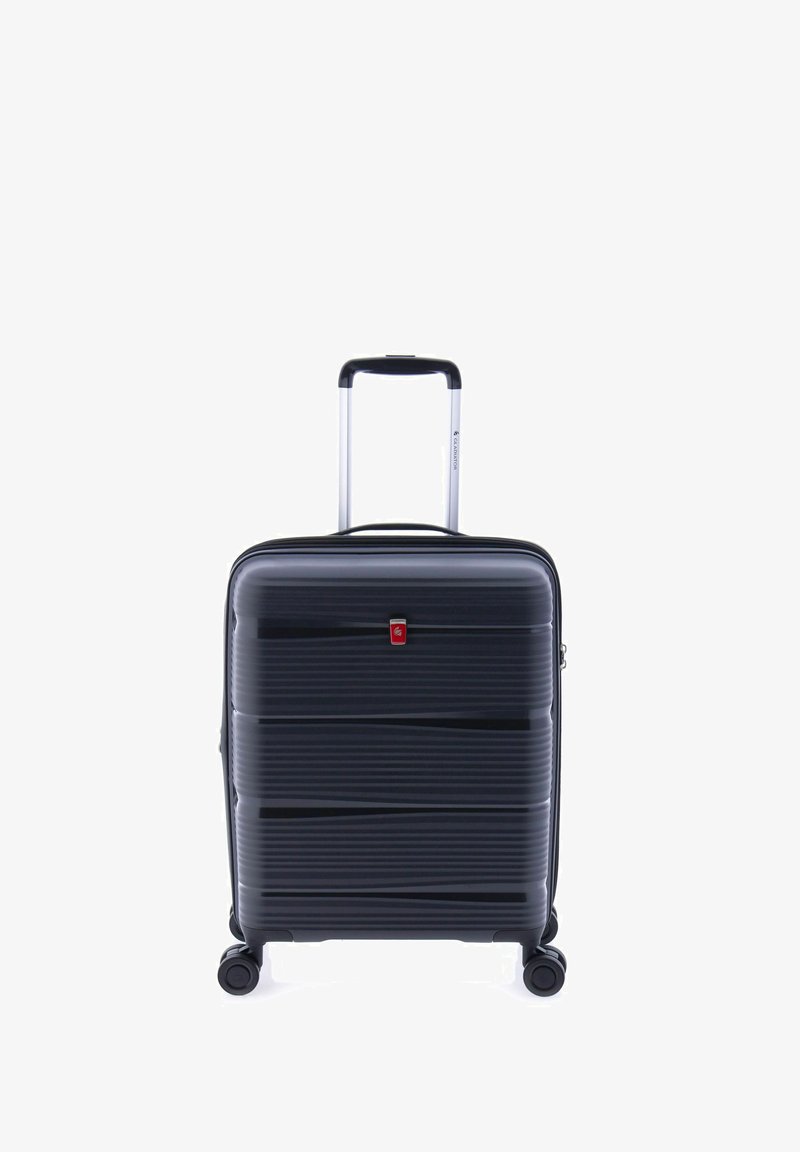 Valigia rigida nera con scanalature orizzontali, manico in alluminio estensibile, quattro ruote e un dettaglio logo rosso sulla parte anteriore.