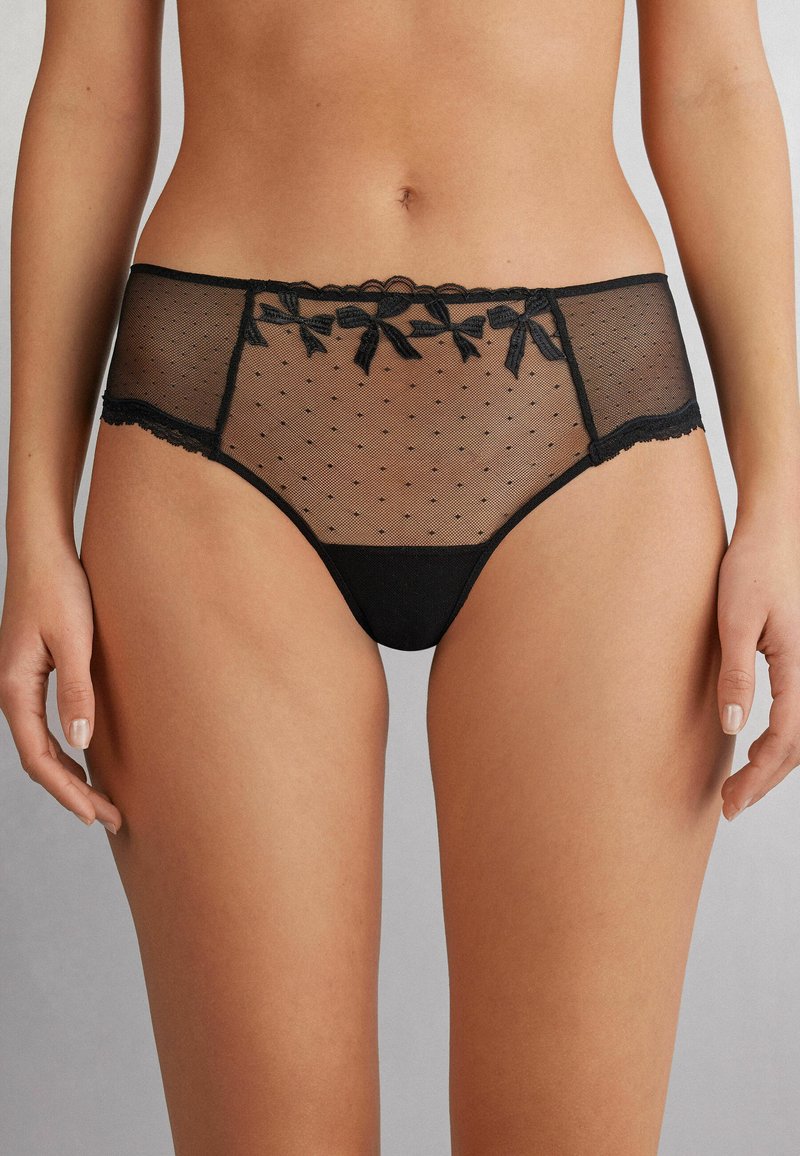 Zwarte lingerie met transparant gaas en polka dots, kantafwerking en decoratieve strikjes op de tailleband. Zachte, lichte stof.