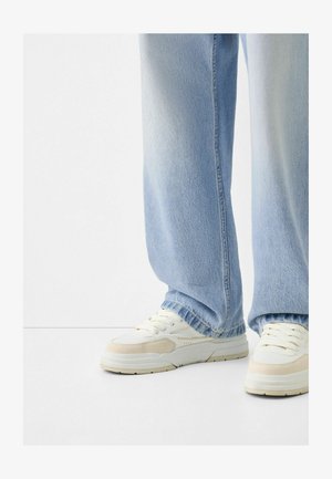 Light blue denim pants with a relaxed fit and frayed hem, paired with cream-colored sneakers featuring textured accents and laces.