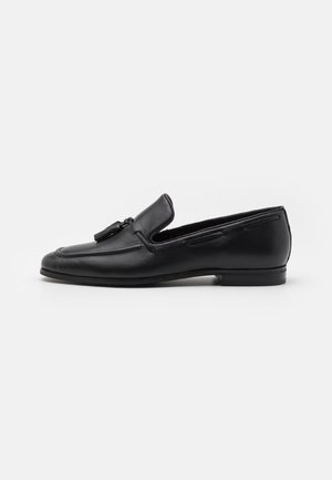 Schwarzer Lederloafer mit abgerundeter Spitze, glattem Finish, Quasten-Akzent und niedrigem Absatz. Seitenansicht zeigt minimalistisches Design und Nahtdetails.