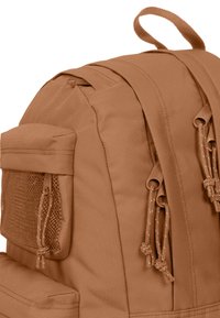 Zaino color tan con tessuto strutturato, tasca frontale in rete, chiusure a coulisse e maniglia superiore per il trasporto.