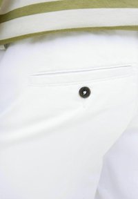 Pantalones de tela blanca con un bolsillo trasero y un detalle de botón oscuro. La textura parece suave con un diseño limpio y a medida.