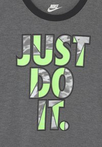 T-shirt in cotone grigio con audace grafica "JUST DO IT" in verde neon e argento riflettente, con scollatura a costine nera.