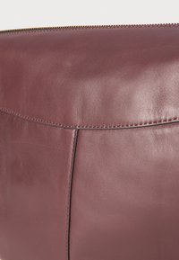 Borsa in pelle bordeaux con texture liscia, forma arrotondata e cuciture visibili lungo la cucitura. Chiusura con zip nella parte superiore.