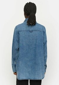 Šviesiai mėlyna džinsinė marškinė, ilgos rankovės, su mygtukų rankogaliais ir šiek tiek ilgesniu nugara. Yra nugaroje peplum ir subtilios siuvimo detalės.