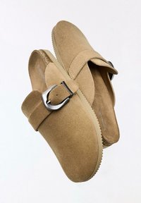 Par beige ruskind uden snørebånd med justerbare sølvspænder og teksturerede beige såler.