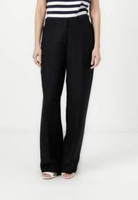 Black wide-leg trousers made of a smooth fabric. Features a flat front and standard pockets. Paired with a striped top and white sandals.