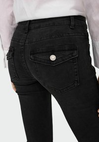 Sorte denimjeans med en tætsiddende pasform, baglommer med skrå flap og en sølvfarvet knapdetalje på taljen.