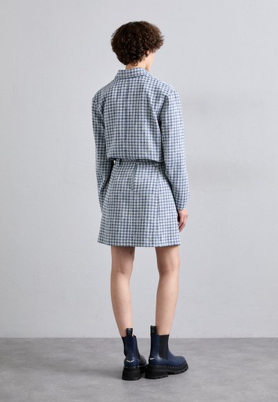 Tkaný modro-biely kabát s vzorom houndstooth, skrátený strih, skombinovaný s rovnakou sukňou. Čierne čižmy na hrubej podrážke dokončujú outfit.